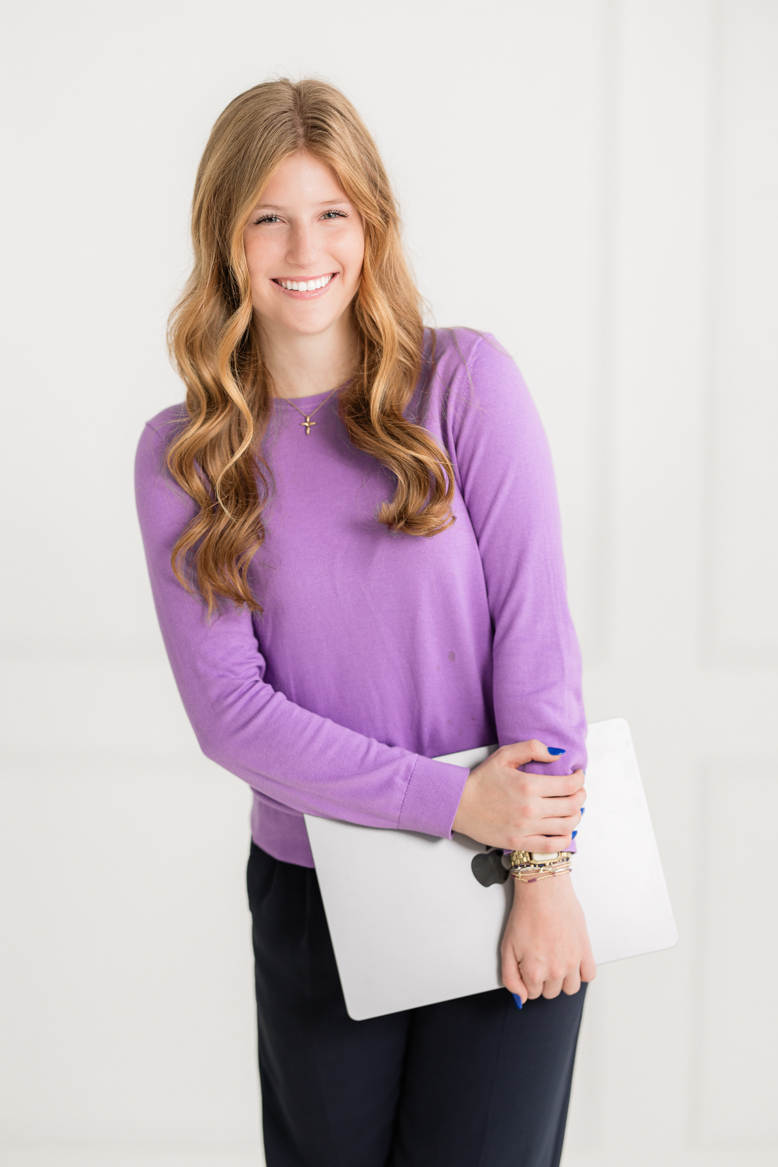 young woman smiling while holding a laptop in a bright studio setting