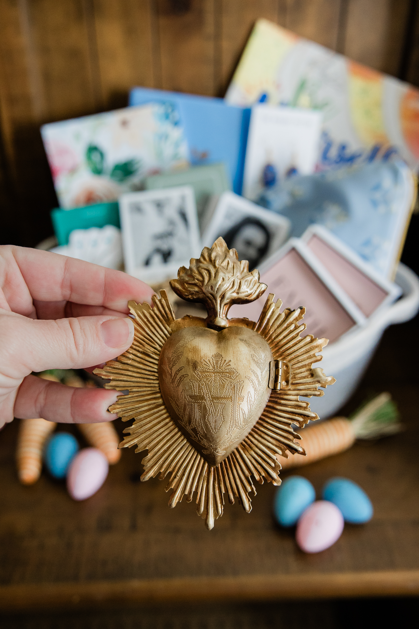 Sacred heart devotional object held in hand with Catholic products in background for ecommerce branding photography.