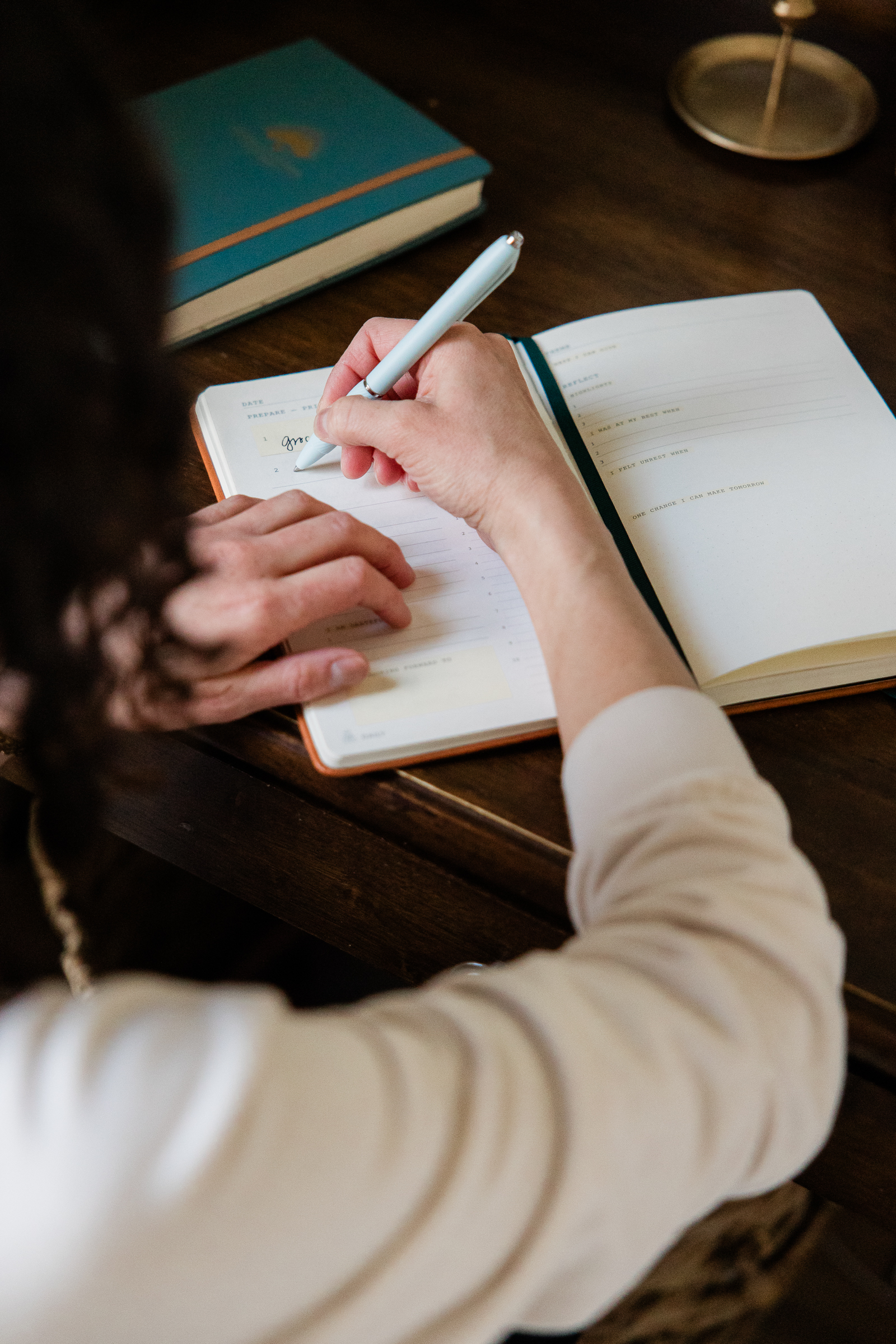 Woman writing in a journal at a wooden desk creating lifestyle imagery for her catholic shop