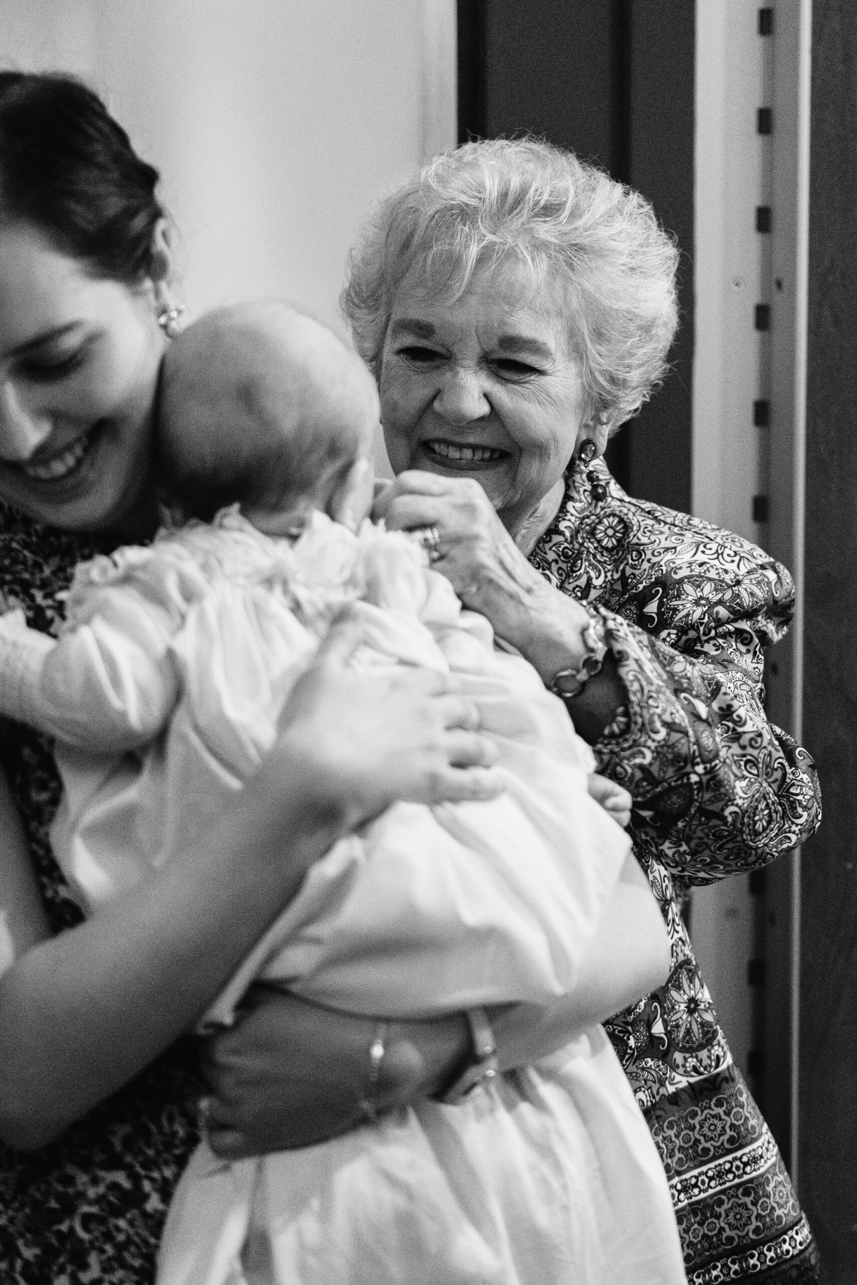 Grandmother embracing a baby after a baptism, candid family moment by a Catholic photographer