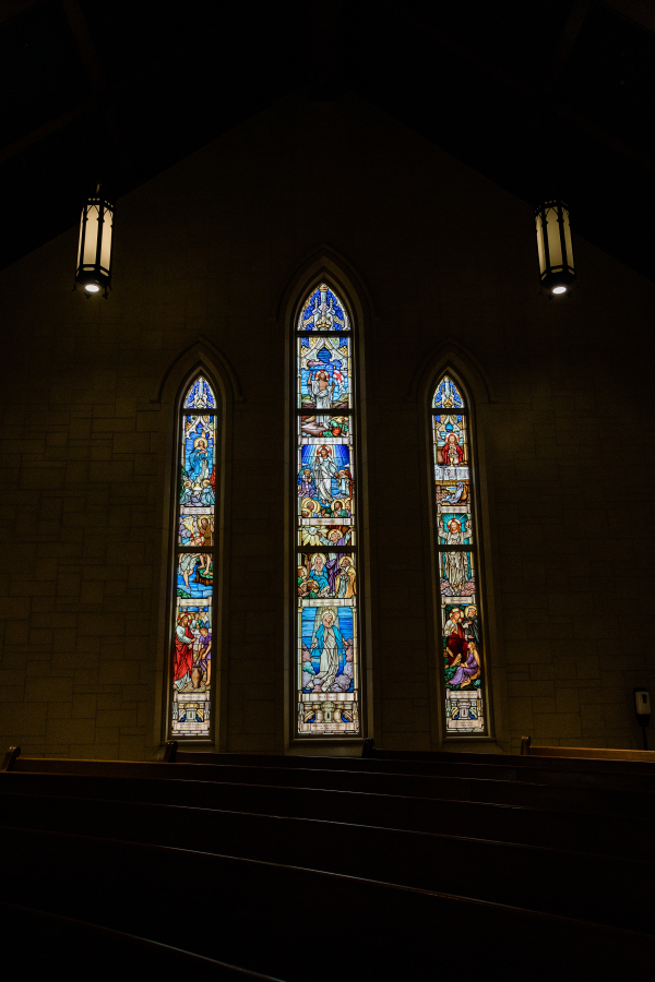 Gothic stained glass windows glowing in a darkened church, photographed by a Catholic photographer